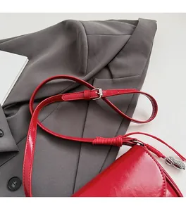 Détail du sac selle rouge brillant avec pendentif cacahuète argenté sur une veste grise