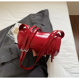 Detail of burgundy cylinder bag with glossy finish and stylish silver metallic buckles