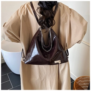 Macro detail of glossy dark brown tote bag with metallic chain and heart pendant accessory