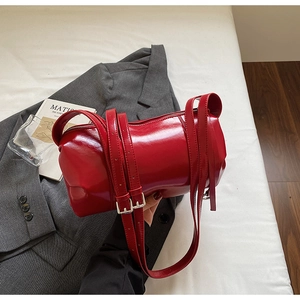 Close-up of bright red glossy cylindrical bag with silver buckles on a grey blazer