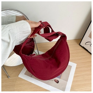 Close-up of burgundy nylon crescent bag with adjustable shoulder strap on wooden desk
