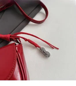 Détail d'un sac à main en cuir verni rouge avec un pendentif en métal argenté en forme d'arachide