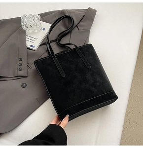 Close-up of black matte leather tote bag with long handles and reinforced bottom stitching