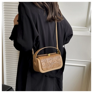 Detail of camel embossed floral crossbody bag with gold hardware on a model