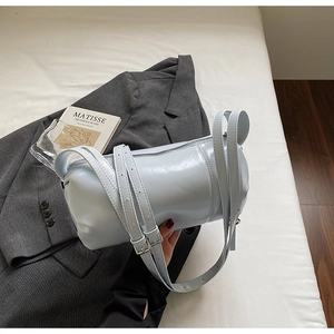 Detail shot of light blue cylindrical barrel bag with adjustable strap on white surface