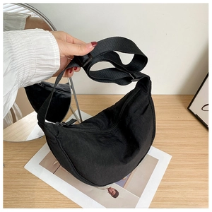 Detail of a black nylon crescent bag with adjustable strap on a minimalist wooden table