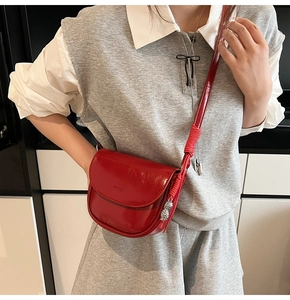 Détail du sac selle en cuir verni rouge avec breloque et logo embossé