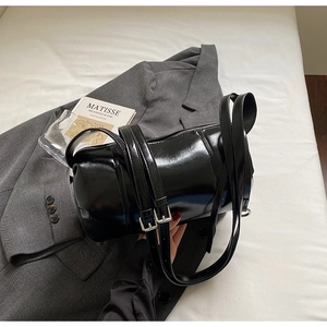 Detail of a shiny black cylindrical shoulder bag on a suit with adjustable straps
