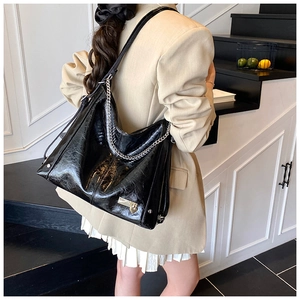 Detail of glossy black vintage tote bag with silver chain and heart padlock on a model