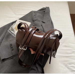 Detail of dark brown glossy cylinder bag with silver buckles on a grey blazer and book