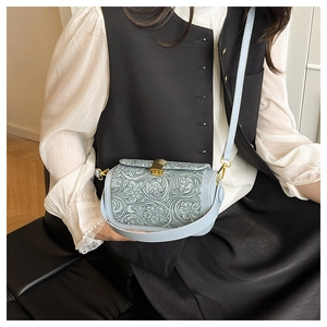 Detail of light blue crossbody bag with vintage embossed floral pattern and shell clasp