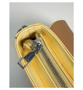 Détail d'un sac à main en cuir jaune clair avec fermeture éclair argentée et coutures