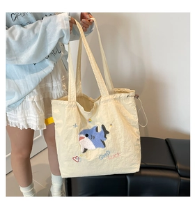 Nahaufnahme der cremefarbenen Canvas-Tasche mit blauer Haifisch-Stickerei und Schrift
