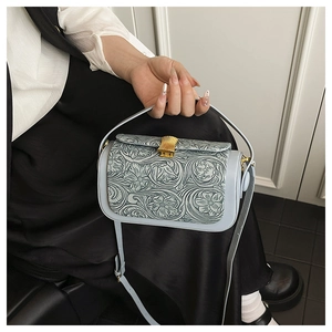 Macro detail of a light blue embossed shoulder bag featuring vintage golden floral lock