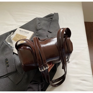 Detail of a brown glossy barrel shoulder bag with silver buckle on a stylish suit