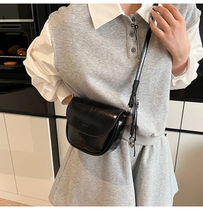 Détail d'un sac besace noir brillant doté d'une bandoulière et d'un pendentif en métal doré