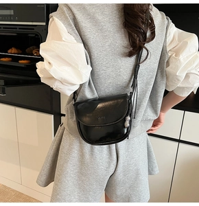 Détail d'un sac selle en cuir noir brillant avec logo LULU et breloque cacahuète argentée