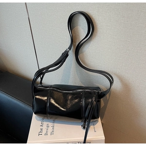 Close-up of glossy black pillow bag with dual zippers placed on white books