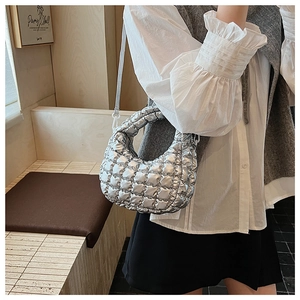 Detail of silver quilted crescent bag with adjustable strap worn by a model in interior