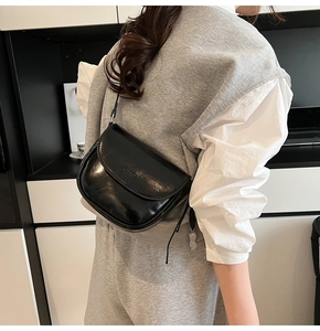 Gros plan d'un sac selle en cuir noir brillant avec texture et bandoulière élégante