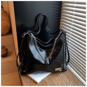 Detail of black glossy leather tote bag featuring a silver chain and heart metal buckle