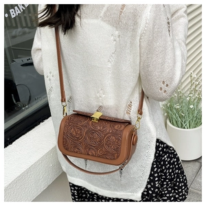 Detail of vintage brown cylindrical crossbody bag featuring embossed floral flap and gold clasp
