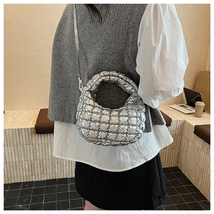 Detailed view of silver quilted puff bag with metallic texture shown in casual indoor setting
