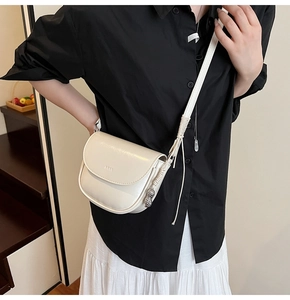 Gros plan d'un sac selle blanc avec pendentif cacahuète argenté et logo embossé