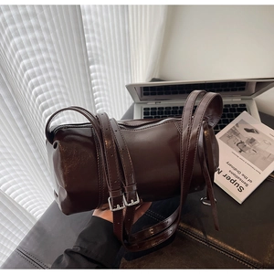 Detail of dark brown cylindrical leather crossbody bag with silver buckles and dual straps
