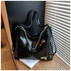 Detail of glossy black hobo bag with thick metal chain and heart charm decoration