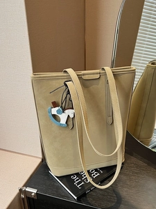 Khaki suede tote bag with long handles and a Trojan horse charm on a dark desk
