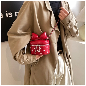 Polka dot mini crossbody bag with a large bow and chain strap shown on a beige coat