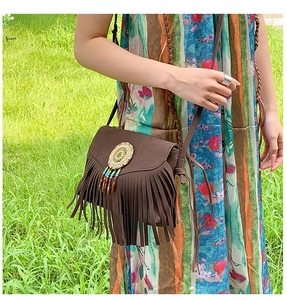 Detail of dark brown suede shoulder bag featuring bohemian tassels and woven disc charms