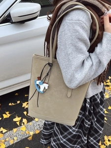 Khaki large capacity tote bag with horse charm shown on model in outdoor autumn setting