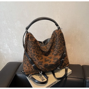 Detail of leopard print tote bag with black faux leather straps on a dark sofa background
