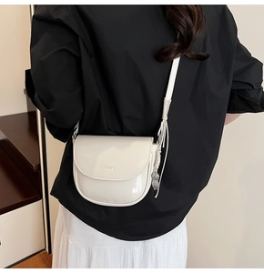 Gros plan sur le sac selle en cuir verni blanc avec breloque cacahuète argentée et sangle