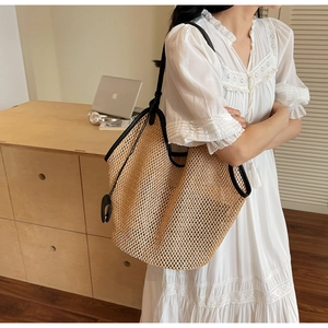 Detail of a large straw tote bag with black trim worn by a model in a modern office setting