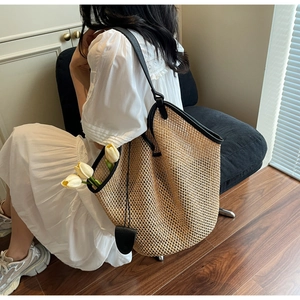 Detail of hollow woven straw tote bag with black leather straps on a seated model