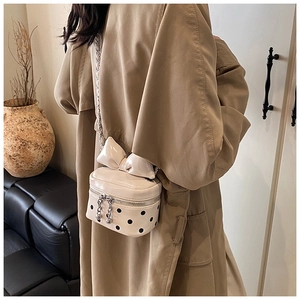Polka dot mini crossbody bag with large bow detail and silver chain strap on a trench coat