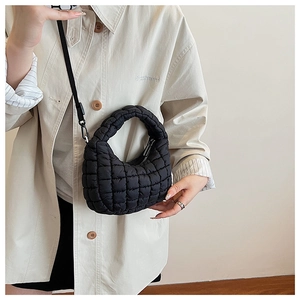Detailed look at the black quilted puffy shoulder bag styled on a female model