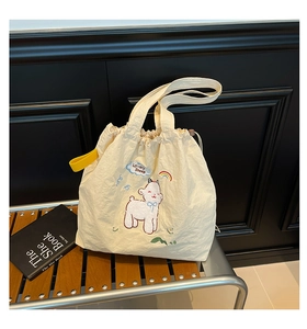Detail einer beigen Zugbeuteltasche mit Schaf-Stickerei und gelben Trägern auf einer Holzbank