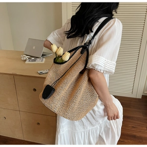 Detail of a woven straw tote bag with black leather trim and round leather charm tag