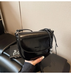 Détail du sac selle en cuir verni noir avec charme métallique et logo embossé