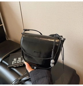 Détail d'un sac besace en cuir noir brillant avec pendentif cacahuète argenté élégant