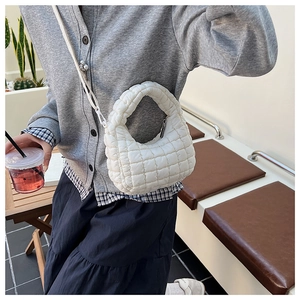 Detailed view of a white quilted puffer bag with crossbody chain worn by a model