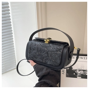 Detail of vintage black leather handbag featuring floral embossing and gold shell clasp