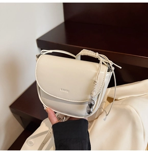 Détail du sac selle blanc crème avec logo LIUUU et pendentif en métal décoratif