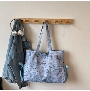 Détail d'un cabas à motif marbre avec des rubans bleus sur un crochet en bois