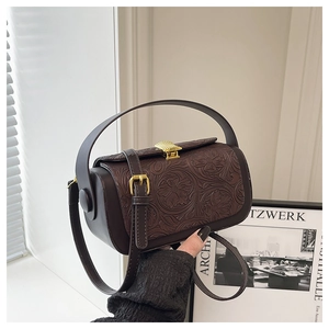 Detail of vintage embossed floral pattern on dark brown leather shoulder bag with gold buckle