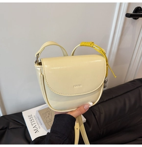 Détail d'un mini sac selle jaune crème en cuir lisse avec bandoulière tressée décorée